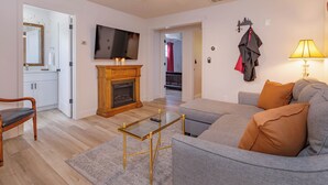 A living room with a grey sofa, a glass coffee table, a wooden cabinet, a fireplace, and a television on the wall. - 2Br Harry Potter Themed Home 7mins from Universal (Orlando)