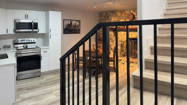 A modern kitchen with white cabinets, stainless steel appliances, and a dining area with a stone wall backdrop. - 2Br Harry Potter Themed Home 7mins from Universal (Orlando)