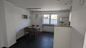 A compact kitchen with a dining area, a window with blinds, and a small potted plant on the counter.