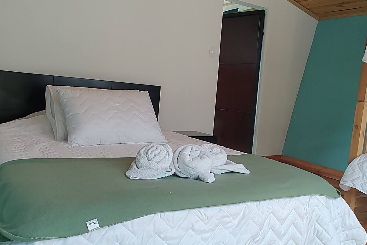 Un plafond en bois, un lit recouvert d’une couverture verte et un couvre-lit blanc matelassé.