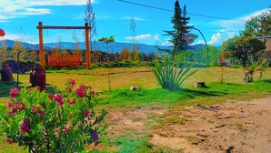 A garden with a swing set, a barbecue grill, and a variety of plants and flowers. - LA TATA CABAÑA  ZON DE CAMPING  (Cucunubá)