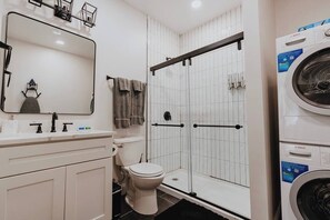 Un baño con inodoro, lavamanos, espejo, ducha con puerta de cristal y lavadora Bosch.