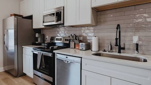 A modern kitchen with stainless steel appliances, white cabinetry, and a tiled backsplash.