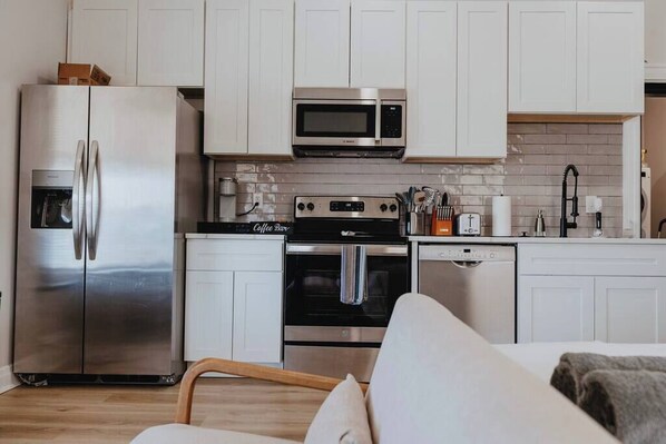 A modern kitchen with white cabinets, stainless steel appliances, and a coffee bar. - Ground-Level Smart-Lock Studio · Walk to SSM-SLU Hospital · Rear-Lot Parking (St. Louis)