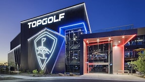 A modern building with a prominent 'TOPGOLF' sign, large glass windows, and a well-lit entrance.