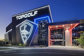 Un edificio moderno con un llamativo letrero de 'TOPGOLF', grandes ventanales de vidrio y una entrada bien iluminada.