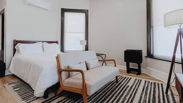 A bedroom with a bed, a sofa, a lamp, and a window.
