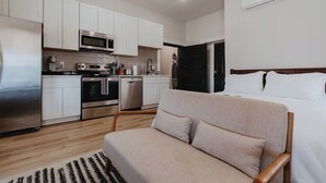Una cocina moderna con armarios blancos, electrodomésticos de acero inoxidable y un comedor con sofá y alfombra.