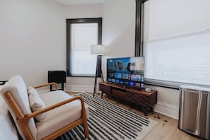 A living room with a sofa, a TV, a lamp, and a radiator. - Ground-Level Smart-Lock Studio · Walk to SSM-SLU Hospital · Free Street Parking (St. Louis)