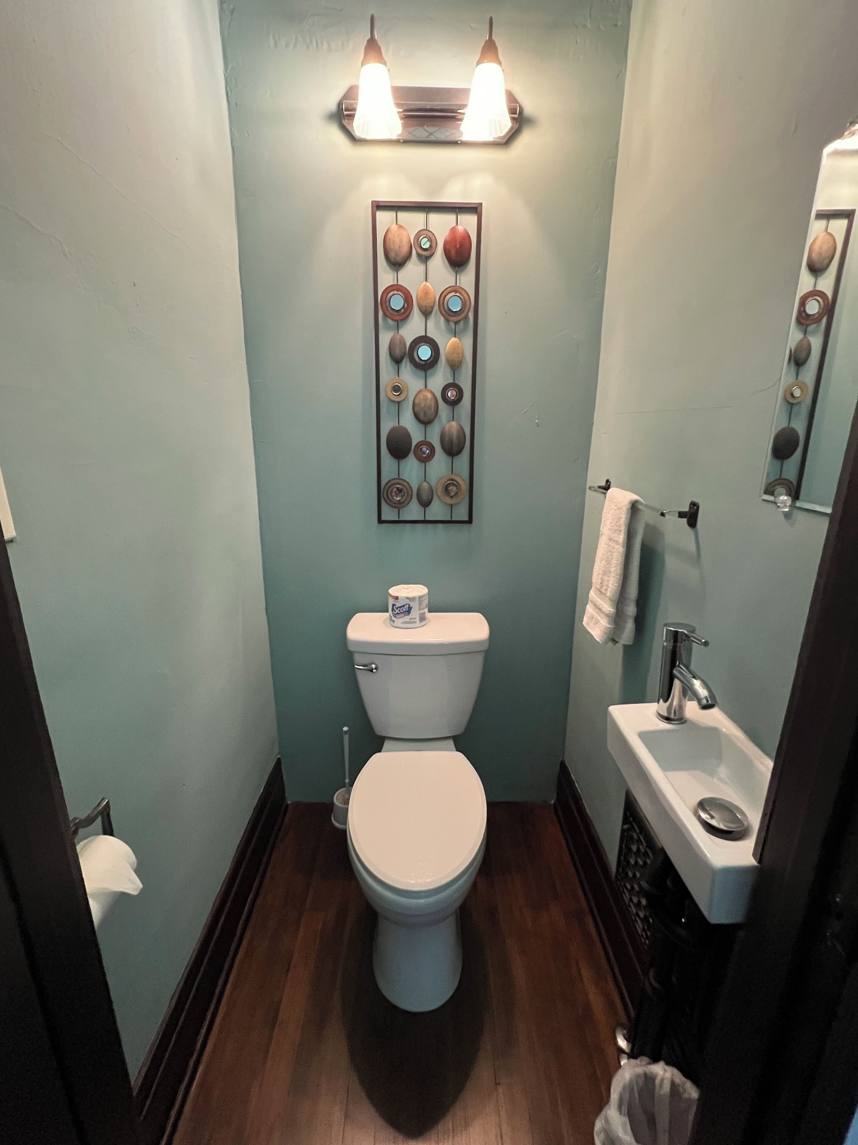 Un baño con inodoro, lavabo, espejo y una lámpara en la pared.
