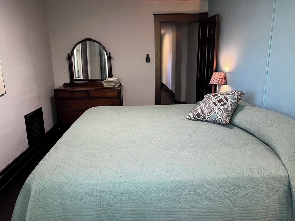 Ein Schlafzimmer mit einem Bett, einem Schminktisch, einem Spiegel und einem Nachttisch mit Lampe.