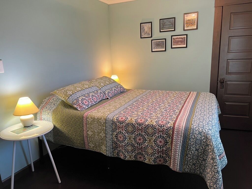 A bedroom with a bed, a bedside table with a lamp, and a door.