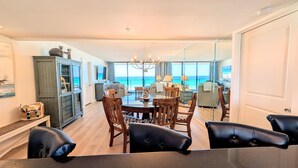 Un comedor con vista al océano, una araña de cristal y un mueble con objetos encima.