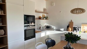 A modern kitchen with white cabinetry, a built-in oven, a sink, and a dining area with a table and chairs.