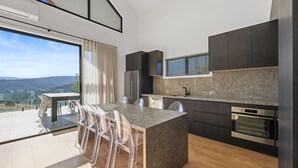 A modern kitchen with dark cabinets, a granite countertop, stainless steel appliances, and a large window overlooking a scenic view.