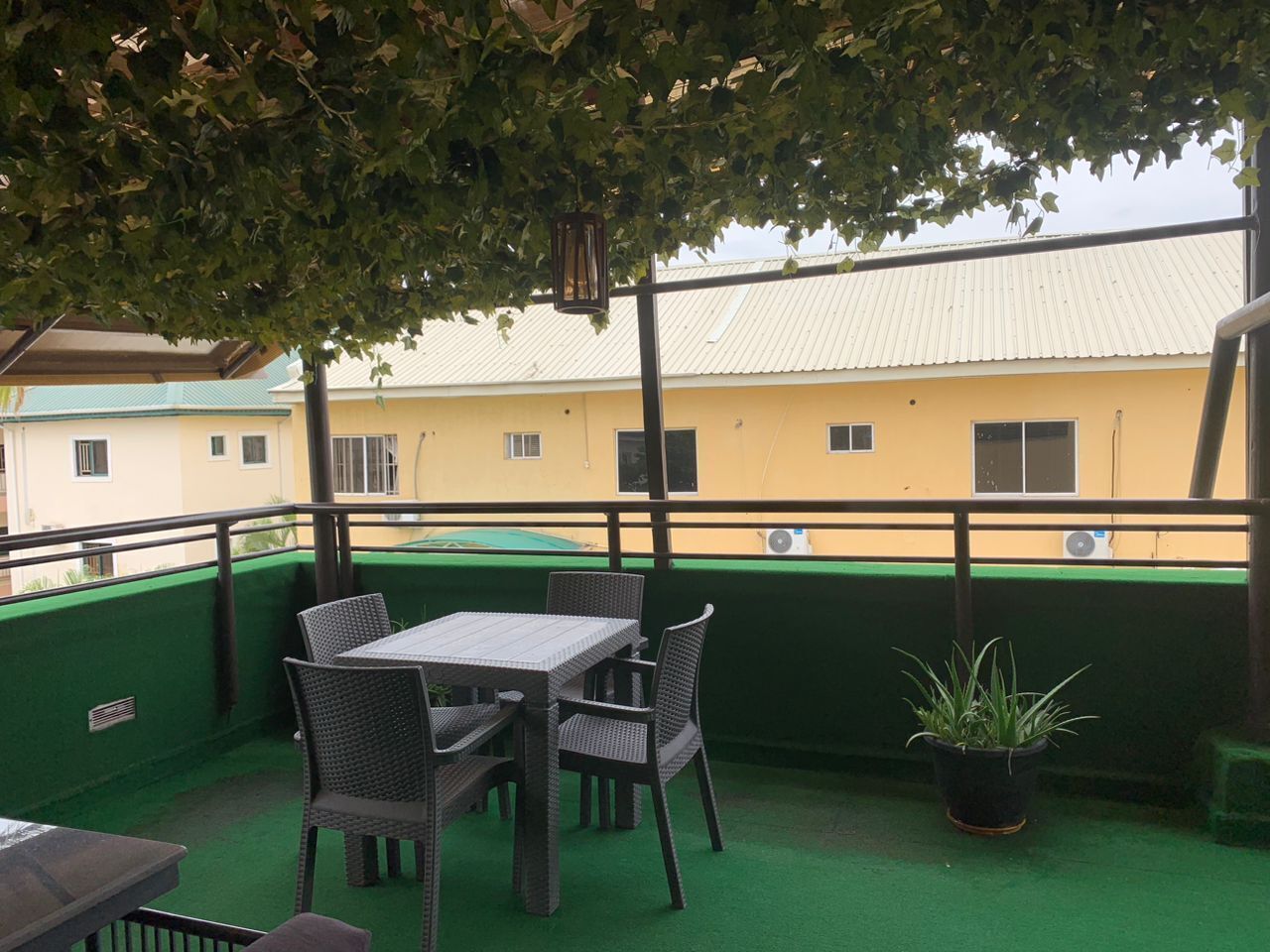 A rooftop terrace with a table and chairs, a potted plant, and a view of a yellow building with multiple windows.