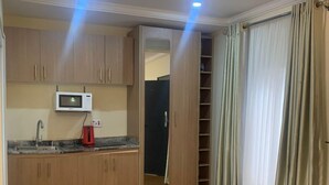 A spacious room with wooden flooring, a built-in kitchen with a microwave, and a large wardrobe with a mirror.