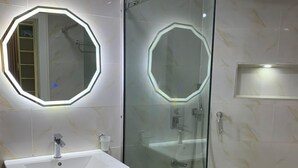A modern bathroom with a glass-enclosed shower, a white sink with a wooden vanity, and two illuminated octagonal mirrors.