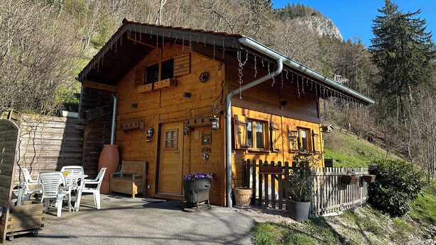 Un chalet en bois doté d’un toit à pente, d’un porche en bois et d’un mur en pierre.