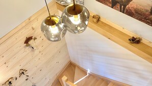 Un intérieur en bois avec un escalier, des luminaires suspendus et un tableau représentant un cerf accroché au mur.