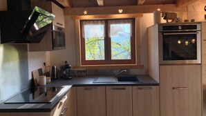 Une cuisine avec des meubles de rangement en bois, une cuisinière, un évier et une fenêtre donnant sur les arbres.