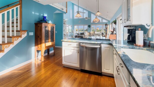 A kitchen with a wooden staircase, white cabinets, a dishwasher, and a large window.