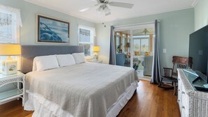 A bedroom with a large bed, two bedside tables with lamps, a ceiling fan, and a view to the outside.