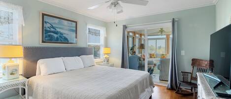 A bedroom with a large bed, two bedside tables with lamps, a ceiling fan, and a view to the outside.