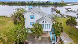 A white house with blue shutters, surrounded by a grassy yard and palm trees, with docks extending into a body of water.