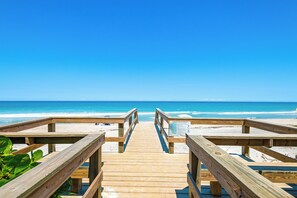 Ein hölzerner Steg führt zu einem Strand bei blauem Himmel.