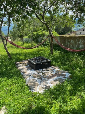 A hammock tied between trees, a fire pit, and a stone pathway in a lush green area. - Gudauri Deka House (Gudauri)