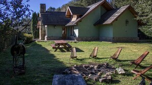 Uma cabana rústica com chaminé de pedra, um deck de madeira e um braseiro.