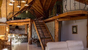Amplo espaço de estar estilo loft, com pé direito alto, vigas de madeira, escada e um espaço de estar aconchegante.
