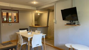Une pièce comprenant une table à manger, des chaises, un téléviseur fixé au mur et une petite table avec des tabourets.