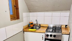 Une cuisine de taille réduite, équipée d’une cuisinière à gaz, d’un évier et de meubles blancs.