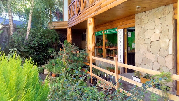 Un edificio rústico de madera con pared de piedra y un balcón. Hay plantas en macetas y una valla de madera en primer plano.