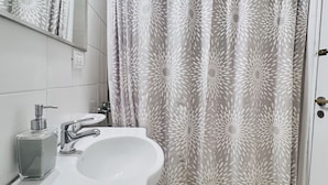 Un baño con un lavamanos blanco, un espejo y una cortina de ducha con diseño de hojas.