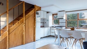 Eine moderne Küche mit weißen Schränken, einer Holztreppe und einem großen Fenster mit Blick auf Bäume.
