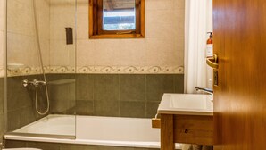 Ein Badezimmer mit Duschkabine aus Glas, einem Fenster mit Holzrahmen und einem weißen Waschbecken.