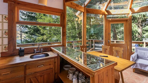 Una cabaña de madera con una zona de cocina que incluye un lavamanos, armarios y una mesa con cubierta de vidrio.