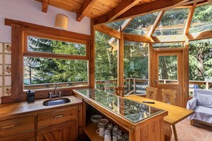 A wooden cabin with a kitchen area featuring a sink, cabinets, and a glass-top table.