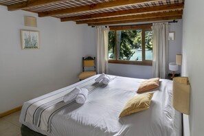 A neatly made bed with towels, a window with curtains, a bedside lamp, and a framed picture on the wall.