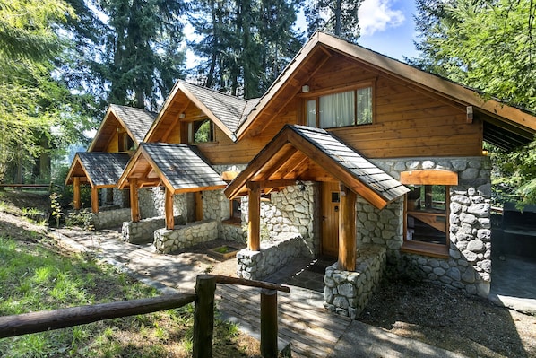 A row of log cabin-style cabins with stone foundations, wooden roofs, and large windows.