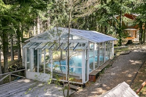 A glass greenhouse with a pool, surrounded by trees.