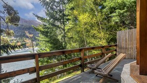 Una terraza de madera con un banco que da a un lago, rodeado de árboles y montañas.