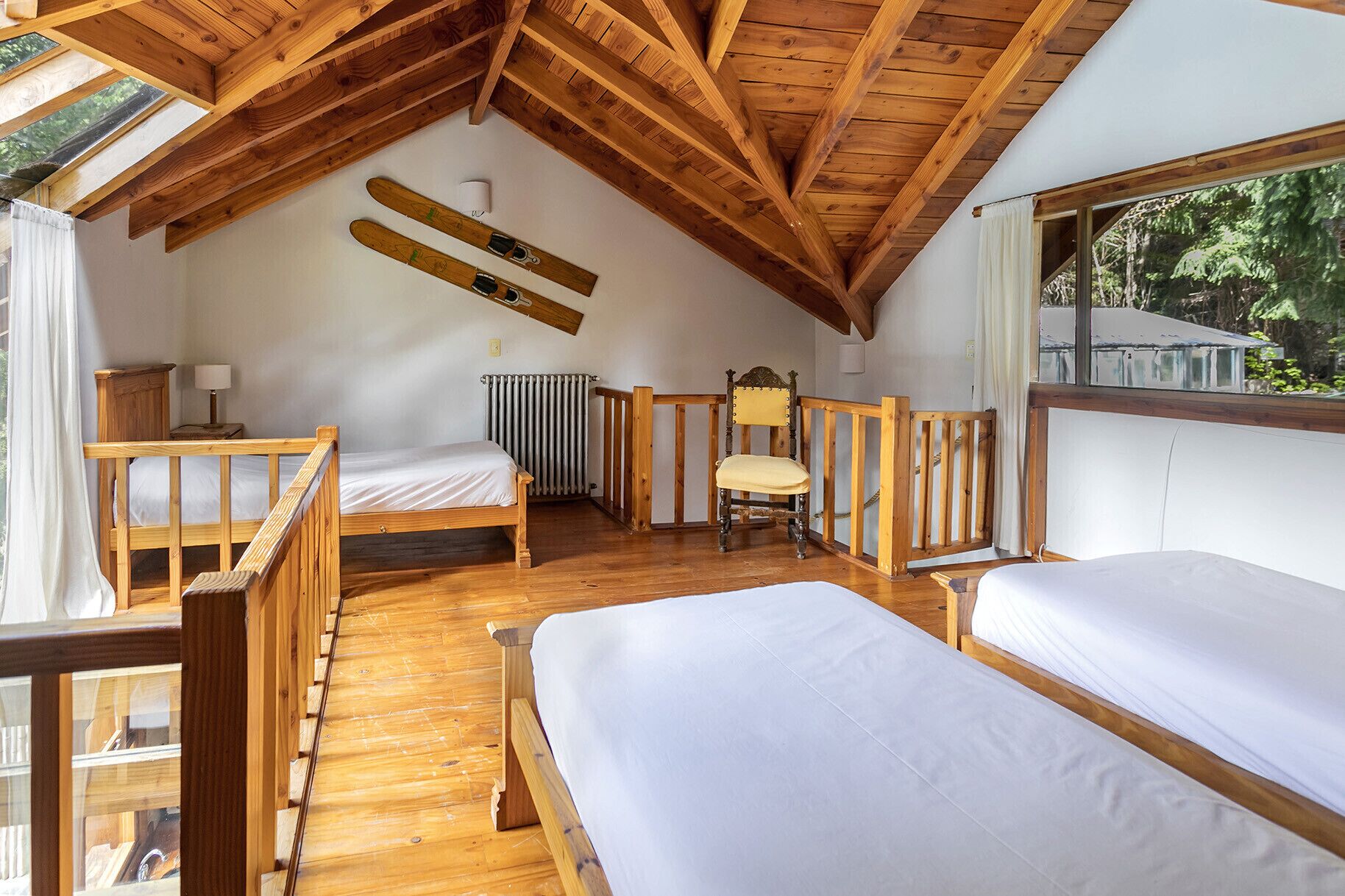 Un dormitorio acogedor en el ático con vigas de madera, una cama, una silla y una ventana con vistas a la vegetación.