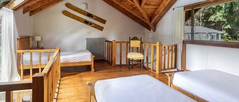 Un dormitorio acogedor en el ático con vigas de madera, una cama, una silla y una ventana con vistas a la vegetación.