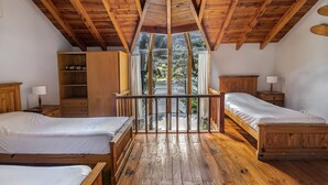 Un dormitorio con dos camas de madera, un armario de madera y un balcón con vistas a árboles.