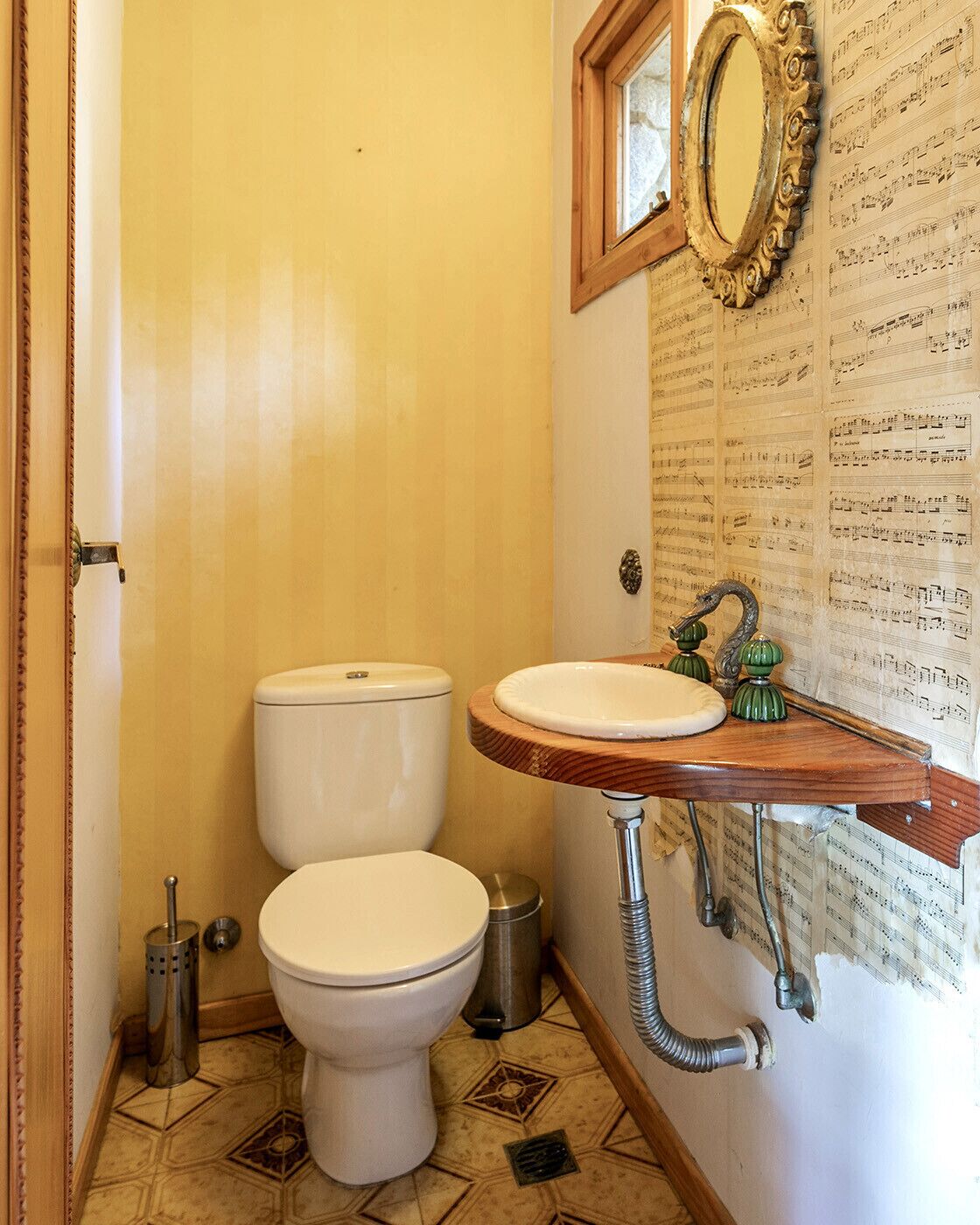 A bathroom with a wooden vanity, two toilets, a mirror, and a wall with sheet music.