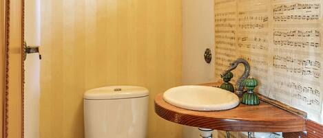 A bathroom with a wooden vanity, two toilets, a mirror, and a wall with sheet music.